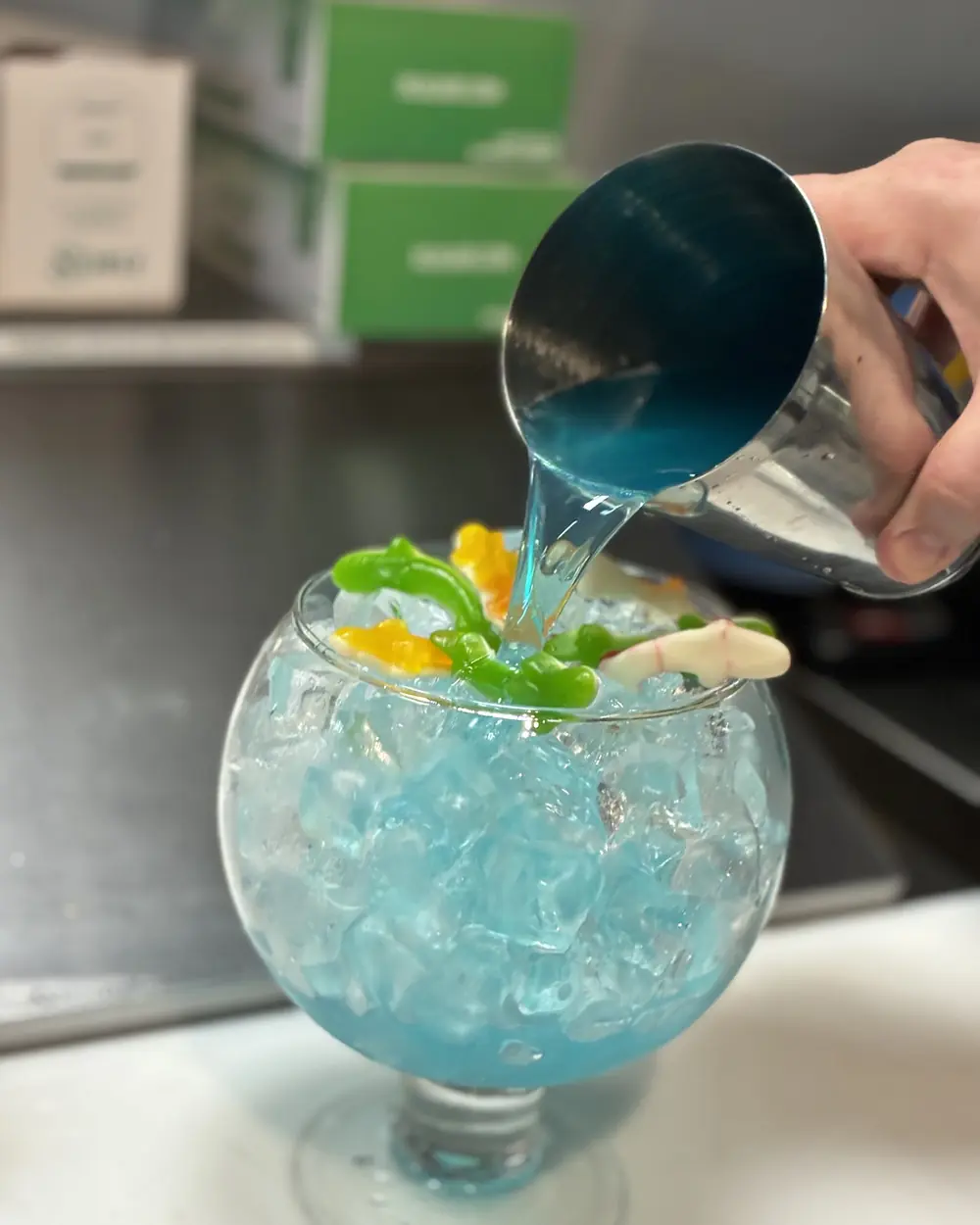A blue fishbowl cocktail being poured at the bar